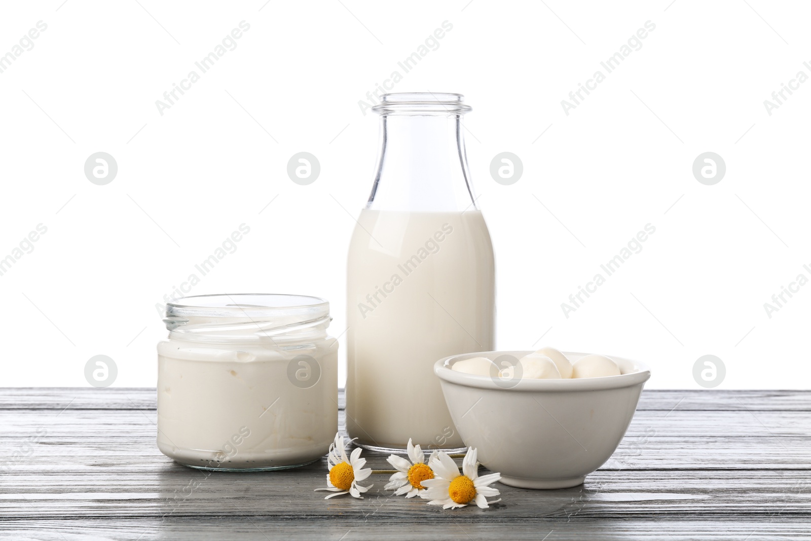 Different fresh dairy products and chamomile flowers on grey wooden table against white background Photo of Different fresh dairy products and chamomile flowers on grey wooden table against white background
