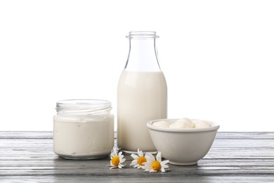 Photo of Different fresh dairy products and chamomile flowers on grey wooden table against white background