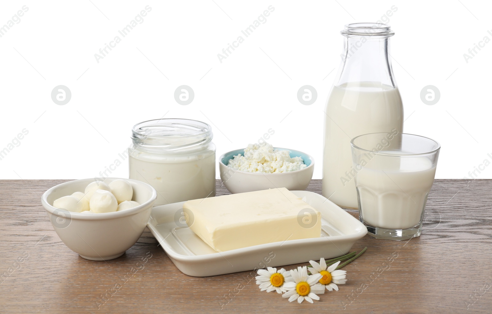 Photo of Different fresh dairy products and chamomile flowers on wooden table against white background