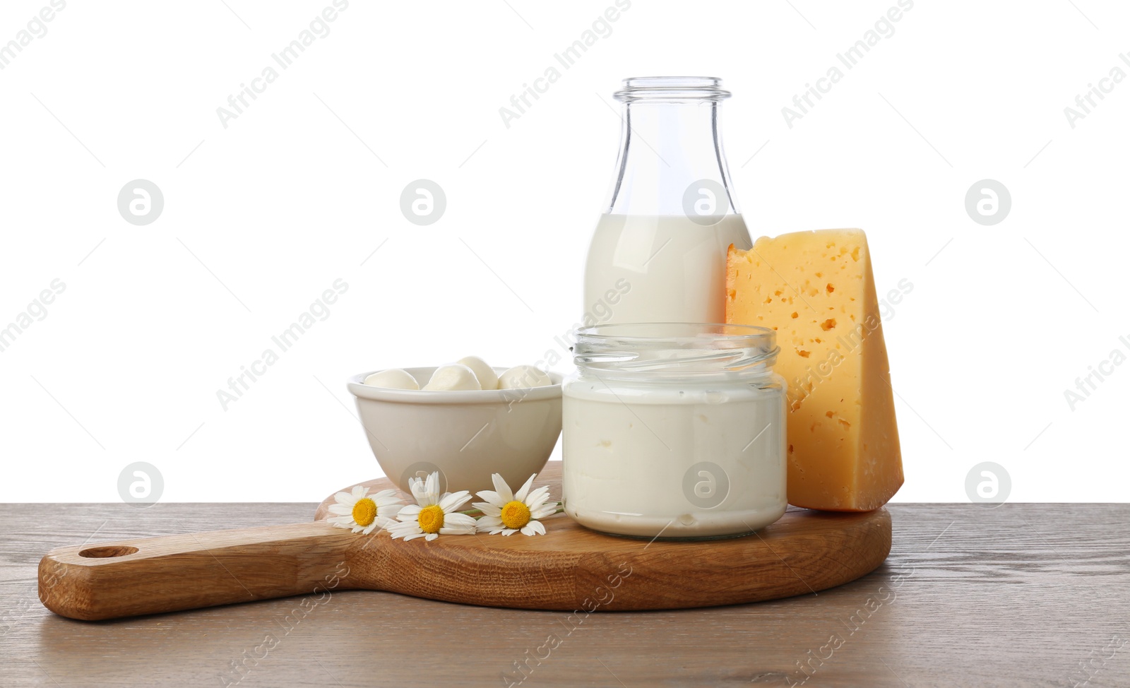 Photo of Different fresh dairy products and chamomile flowers on wooden table against white background