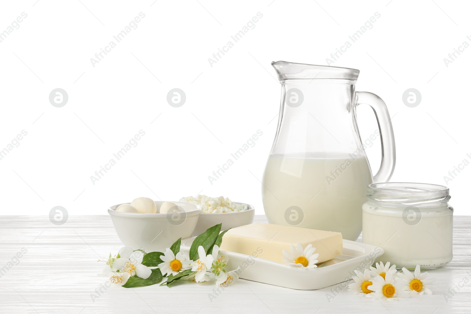 Photo of Different fresh dairy products and flowers on wooden table against white background