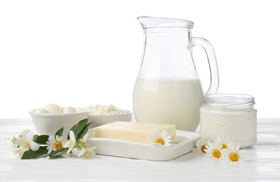 Photo of Different fresh dairy products and flowers on wooden table against white background