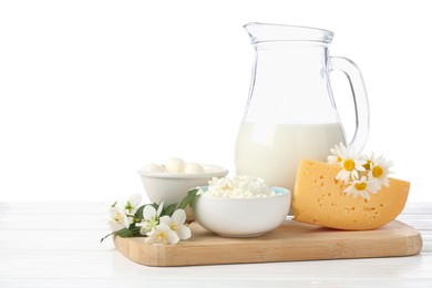 Photo of Different fresh dairy products and flowers on wooden table against white background