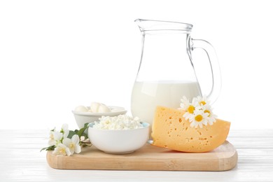 Photo of Different fresh dairy products and flowers on wooden table against white background