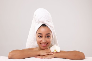 Photo of Portrait of beautiful Brazilian woman with towel and orchid flower after spa treatment on light gray background