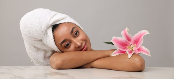 Photo of Portrait of beautiful Brazilian woman with lily flower after spa treatment at light marble table on gray background