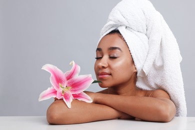 Photo of Portrait of beautiful Brazilian woman with lily flower after spa treatment at light table on gray background