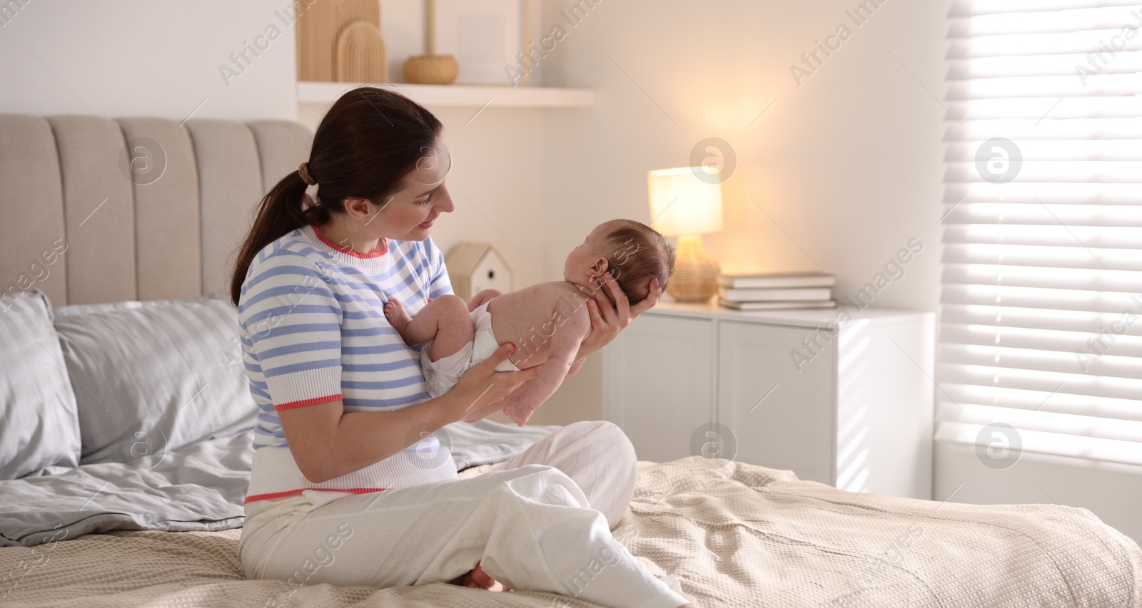 Mother putting her cute newborn baby to sleep on bed at home Photo of Mother putting her cute newborn baby to sleep on bed at home