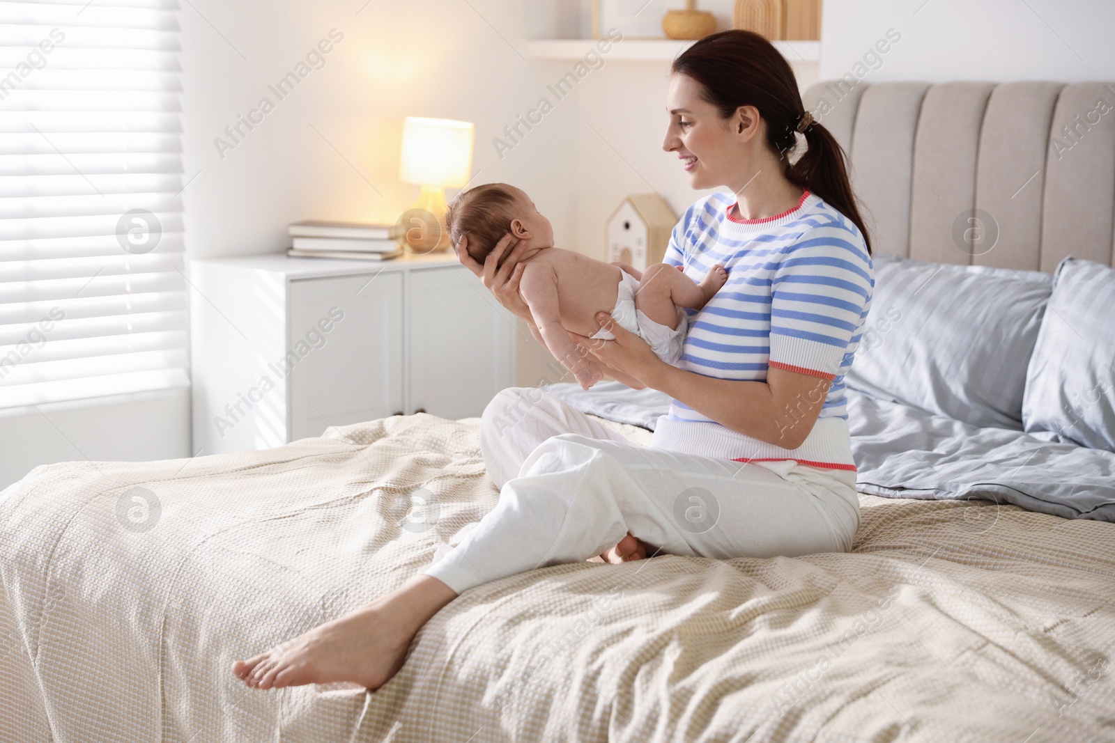 Mother putting her cute newborn baby to sleep on bed at home Photo of Mother putting her cute newborn baby to sleep on bed at home