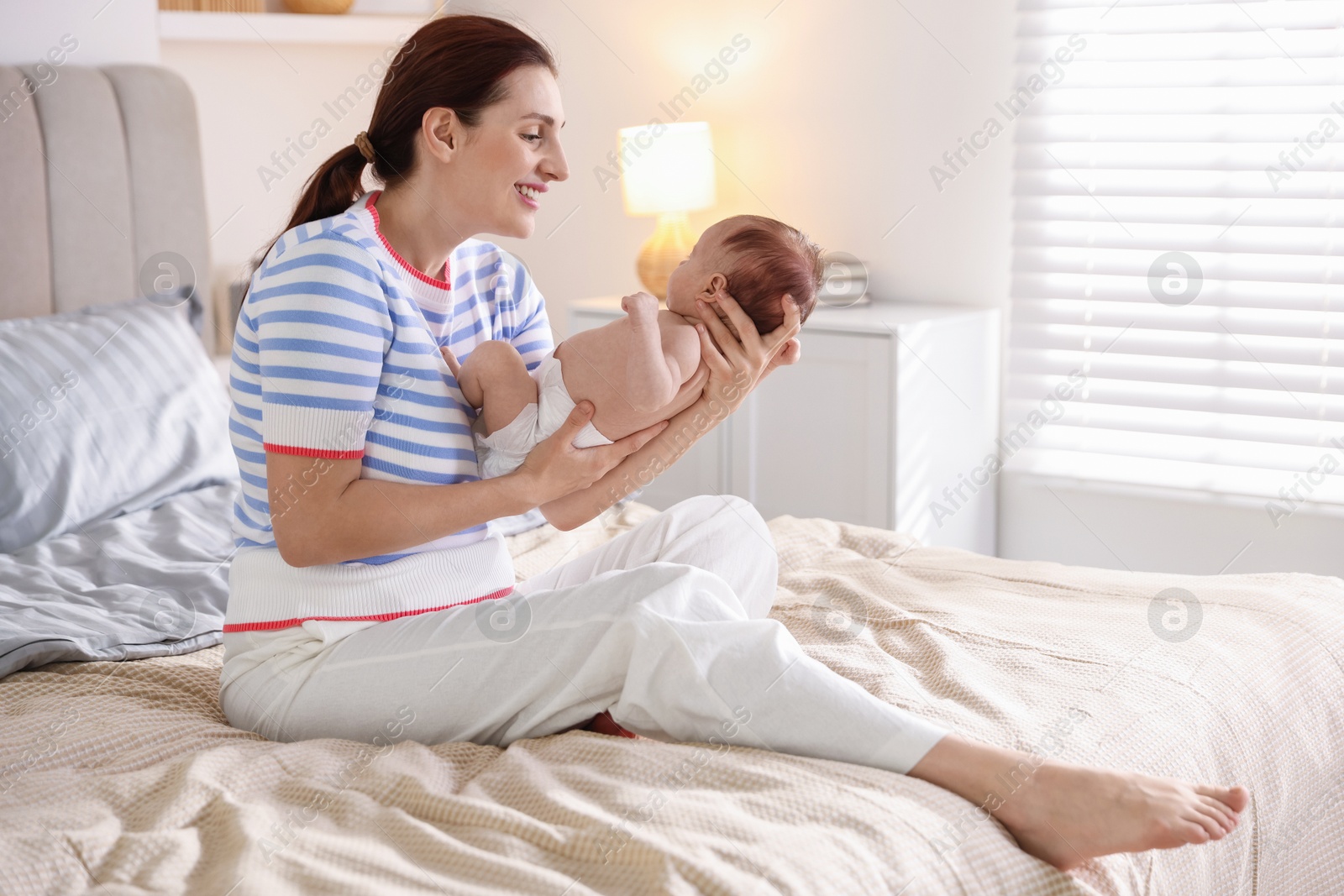 Mother putting her cute newborn baby to sleep on bed at home Photo of Mother putting her cute newborn baby to sleep on bed at home