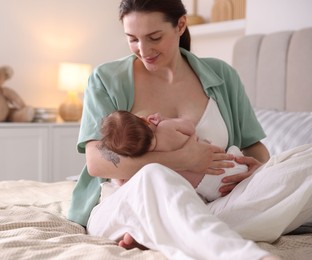 Photo of Mother breastfeeding her newborn baby on bed indoors