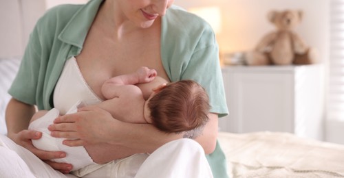 Photo of Mother breastfeeding her newborn baby indoors, closeup. Space for text