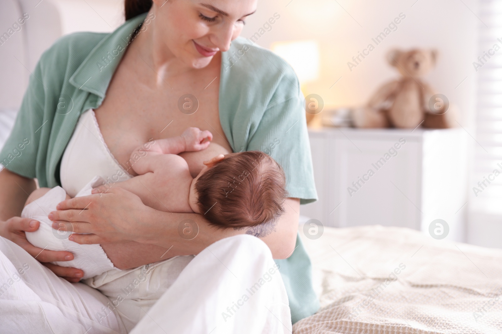 Mother breastfeeding her newborn baby on bed indoors Photo of Mother breastfeeding her newborn baby on bed indoors