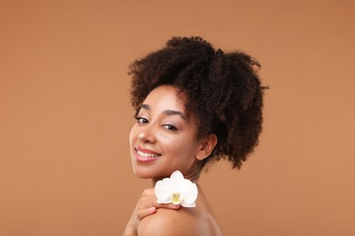 Photo of Portrait of beautiful Brazilian woman with orchid flower after spa treatment on light brown background