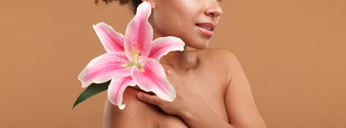 Photo of Brazilian woman with lily flower after spa treatment on light brown background, closeup