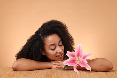 Photo of Portrait of beautiful Brazilian woman with lily flower after spa treatment at bamboo table on beige background