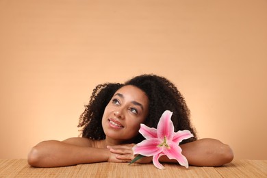 Photo of Portrait of beautiful Brazilian woman with lily flower after spa treatment at bamboo table on beige background