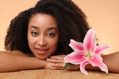 Photo of Beautiful woman with lily flower after spa treatment at bamboo table on beige background, closeup