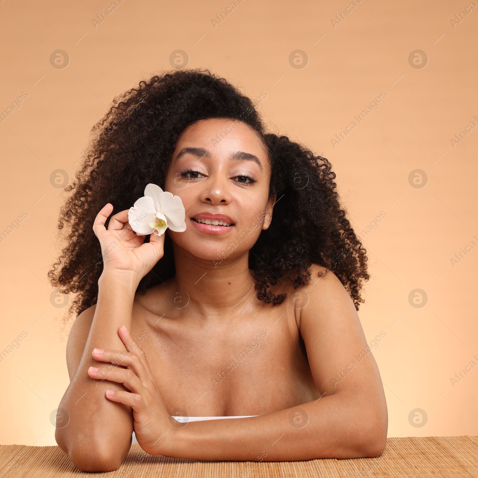 Portrait of beautiful Brazilian woman with orchid flower after spa treatment at bamboo table on beige gradient background Photo of Portrait of beautiful Brazilian woman with orchid flower after spa treatment at bamboo table on beige gradient background