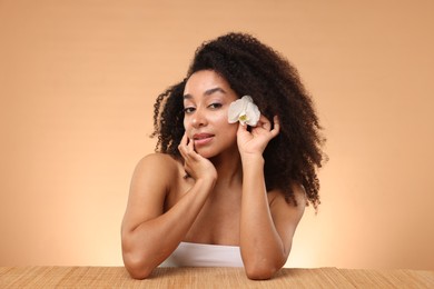 Photo of Portrait of beautiful Brazilian woman with orchid flower after spa treatment at bamboo table on beige gradient background