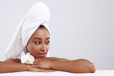 Photo of Portrait of beautiful Brazilian woman with towel and orchid flower after spa treatment on light gray background. Space for text