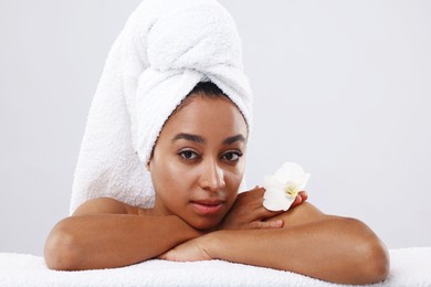 Photo of Portrait of beautiful Brazilian woman with towel and orchid flower after spa treatment on light gray background