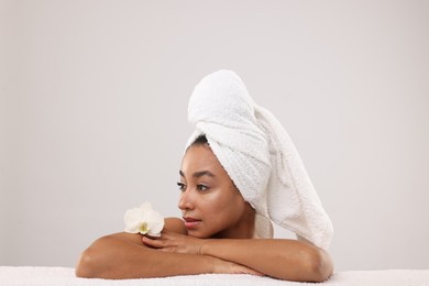 Photo of Portrait of beautiful Brazilian woman with towel and orchid flower after spa treatment on light gray background