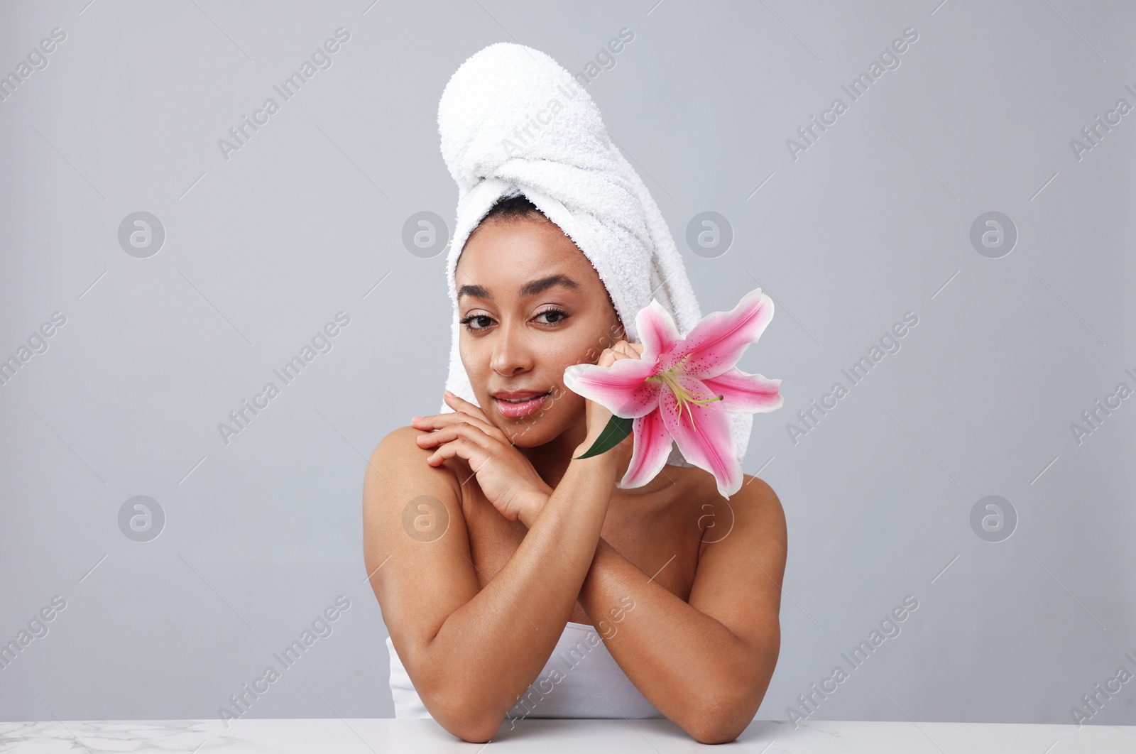 Portrait of beautiful Brazilian woman with lily flower after spa treatment at light marble table on gray background Photo of Portrait of beautiful Brazilian woman with lily flower after spa treatment at light marble table on gray background