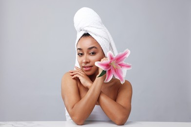 Photo of Portrait of beautiful Brazilian woman with lily flower after spa treatment at light marble table on gray background