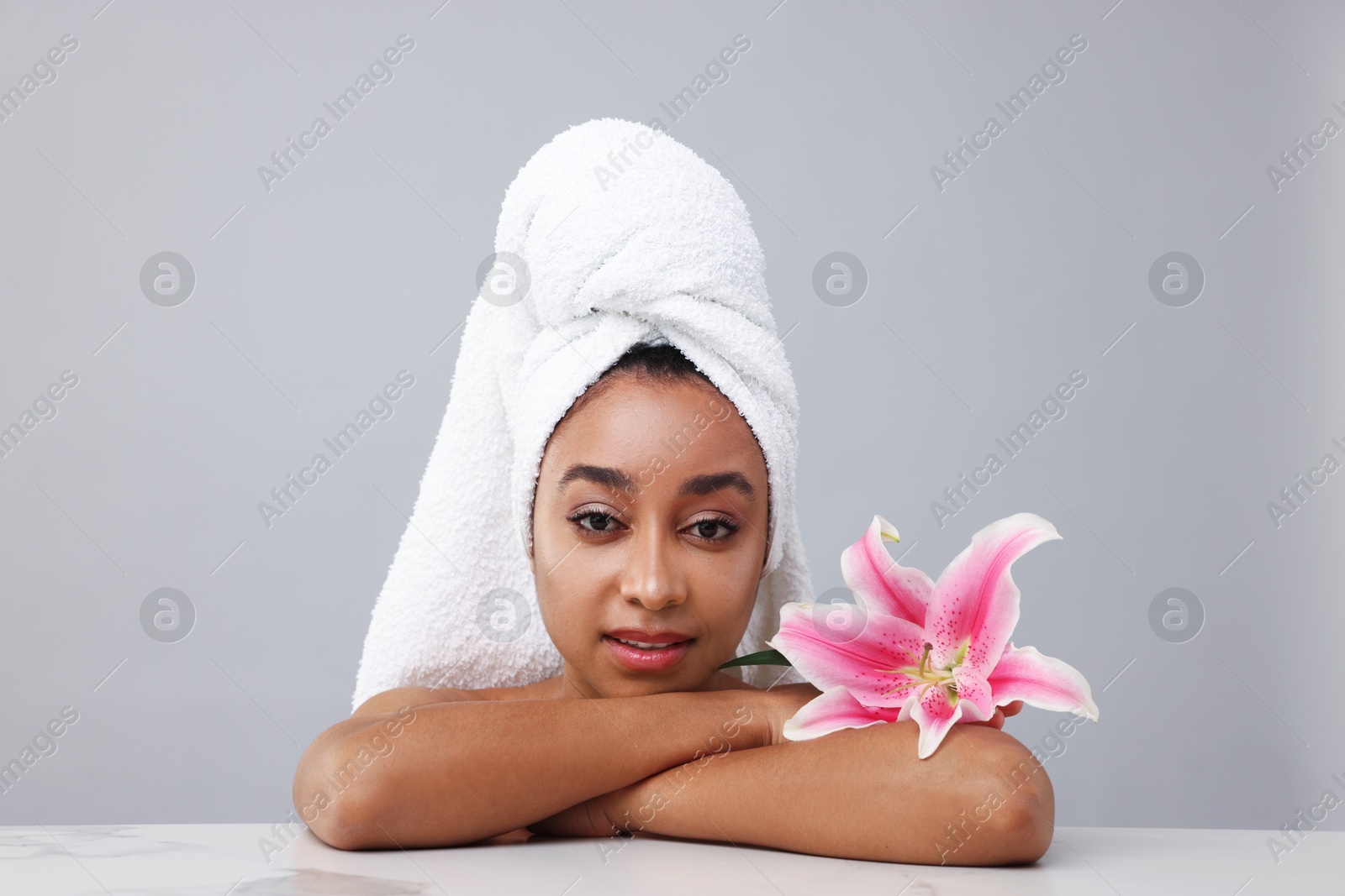 Portrait of beautiful Brazilian woman with lily flower after spa treatment at light marble table on gray background Photo of Portrait of beautiful Brazilian woman with lily flower after spa treatment at light marble table on gray background
