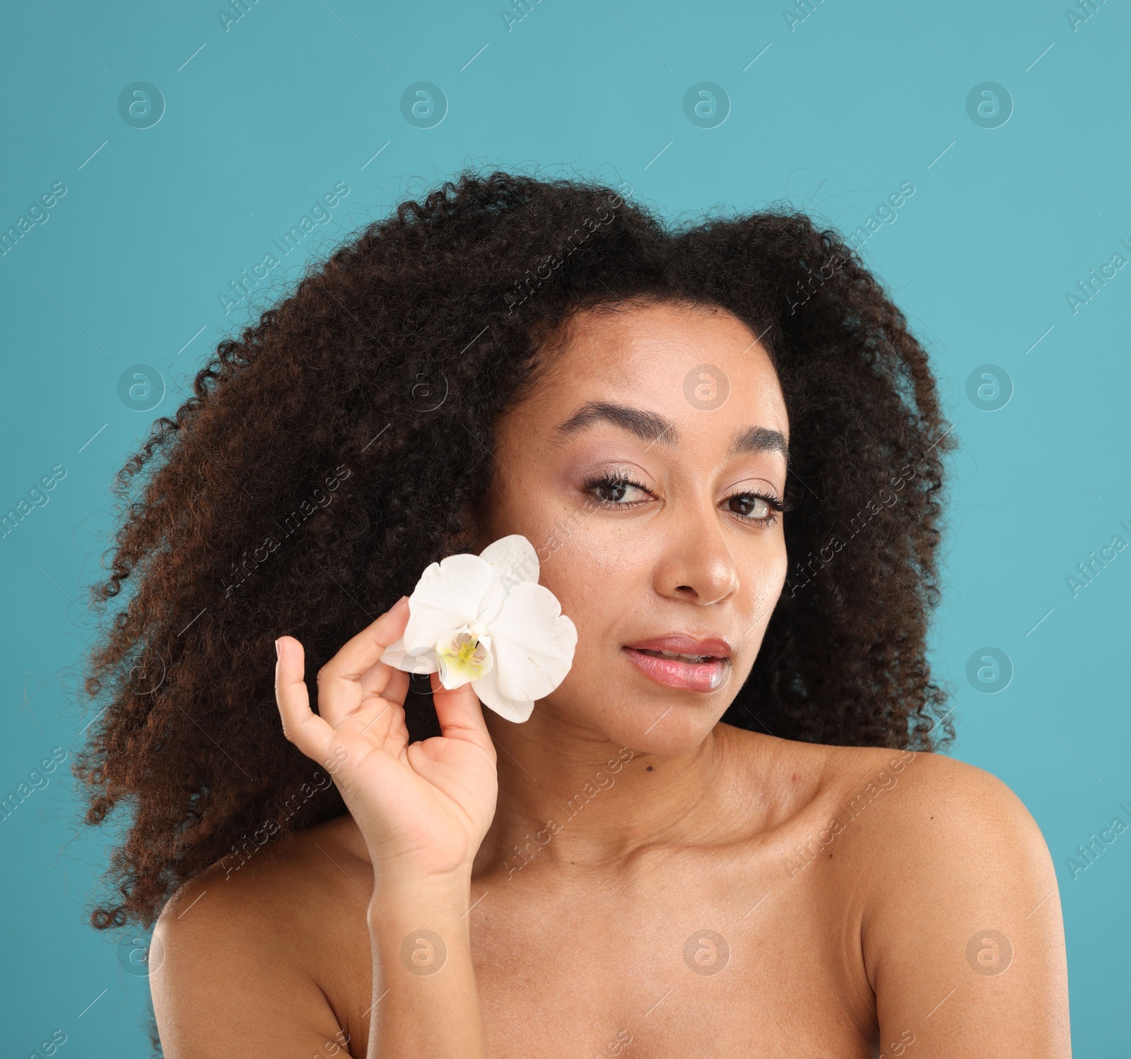 Portrait of beautiful Brazilian woman with orchid flower after spa treatment on light blue background Photo of Portrait of beautiful Brazilian woman with orchid flower after spa treatment on light blue background
