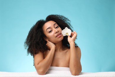 Photo of Portrait of beautiful Brazilian woman with orchid flower and towel after spa treatment on light blue background