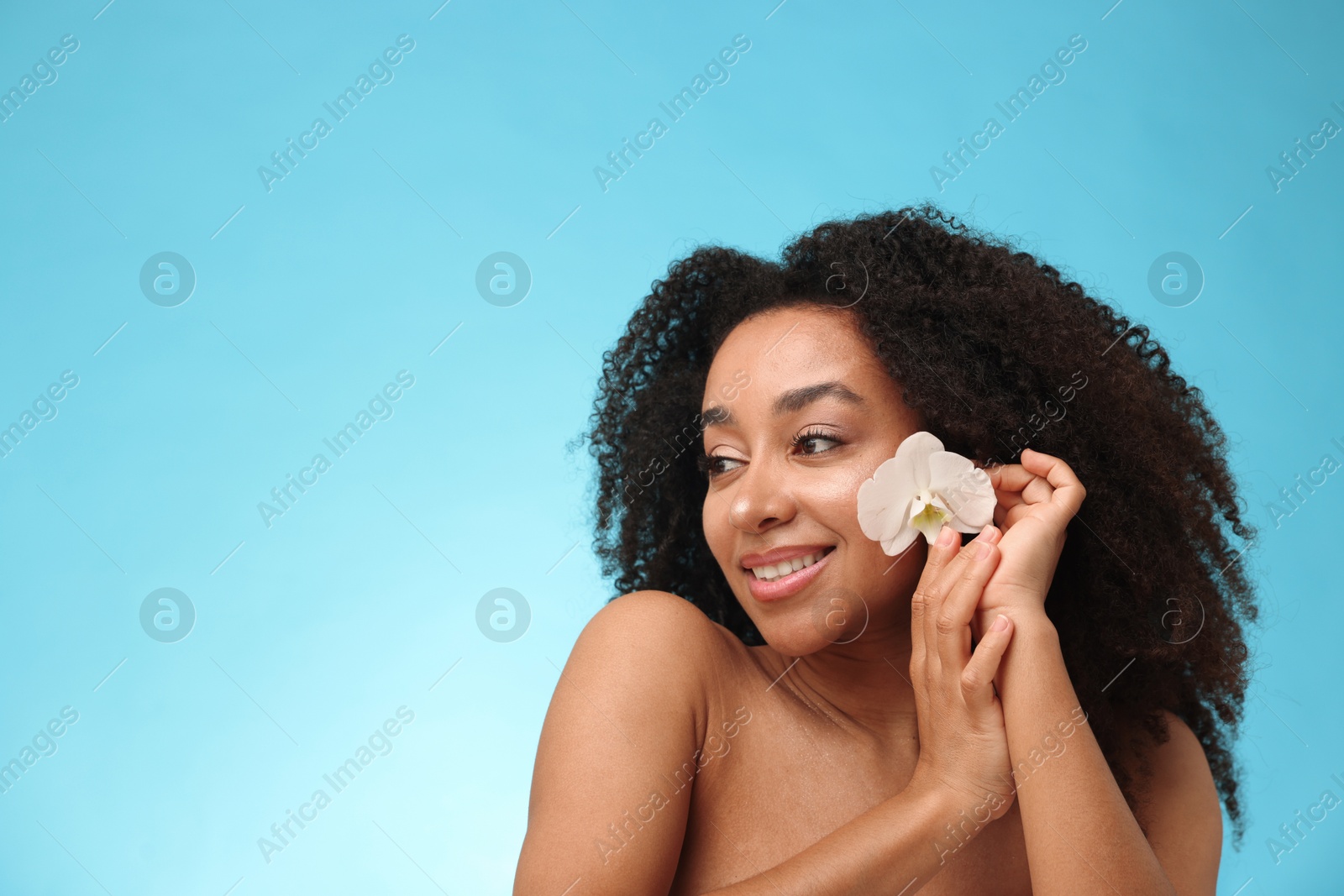 Portrait of beautiful Brazilian woman with orchid flower after spa treatment on light blue gradient background. Space for text Photo of Portrait of beautiful Brazilian woman with orchid flower after spa treatment on light blue gradient background. Space for text