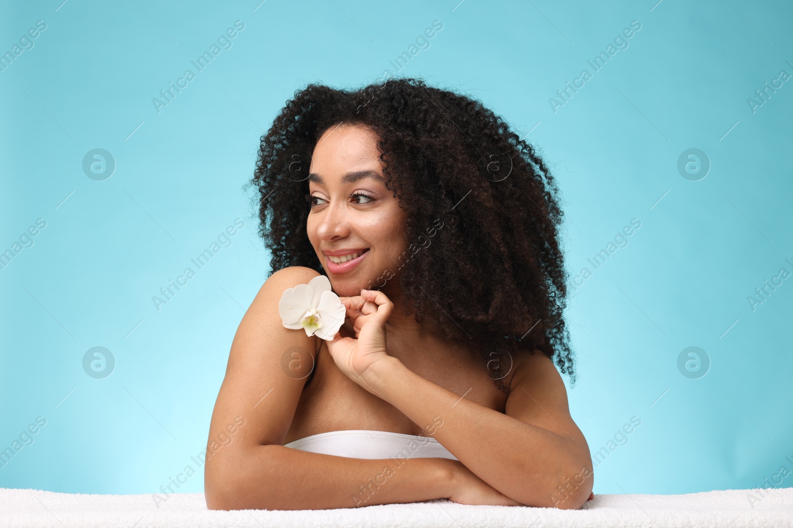 Portrait of beautiful Brazilian woman with orchid flower and towel after spa treatment on light blue background Photo of Portrait of beautiful Brazilian woman with orchid flower and towel after spa treatment on light blue background