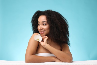 Photo of Portrait of beautiful Brazilian woman with orchid flower and towel after spa treatment on light blue background