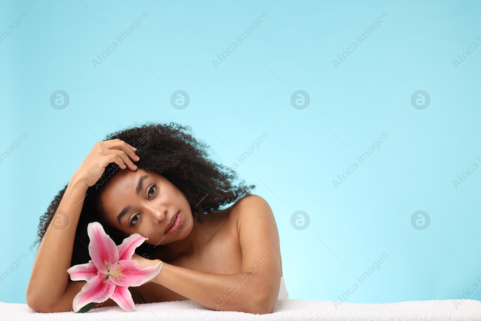 Portrait of beautiful Brazilian woman with lily flower and towel after spa treatment on light blue background. Space for text Photo of Portrait of beautiful Brazilian woman with lily flower and towel after spa treatment on light blue background. Space for text