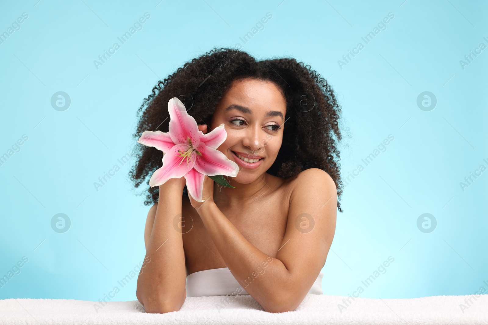 Portrait of beautiful Brazilian woman with lily flower and towel after spa treatment on light blue background Photo of Portrait of beautiful Brazilian woman with lily flower and towel after spa treatment on light blue background