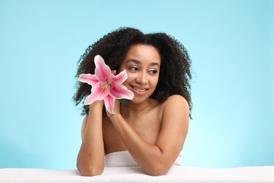 Photo of Portrait of beautiful Brazilian woman with lily flower and towel after spa treatment on light blue background