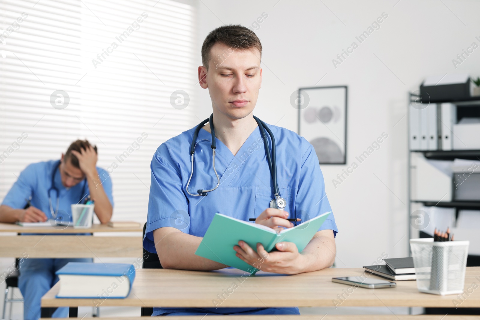 Medical students in uniforms studying at desks indoors, selective focus Photo of Medical students in uniforms studying at desks indoors, selective focus