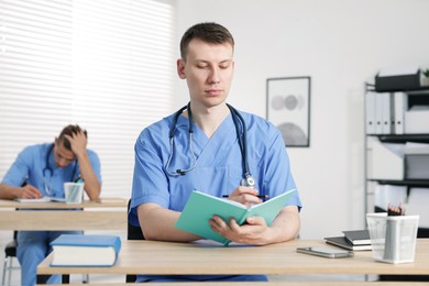 Photo of Medical students in uniforms studying at desks indoors, selective focus