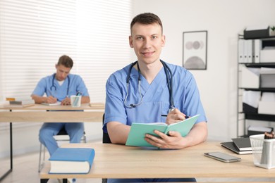 Photo of Medical students in uniforms studying at desks indoors, selective focus