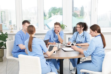 Photo of Medical students in uniforms studying together at table indoors