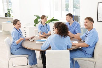 Photo of Medical students in uniforms studying together at table indoors