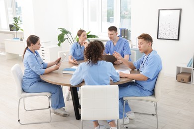 Photo of Medical students in uniforms studying together at table indoors