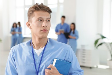 Photo of Medical student in uniform with book indoors, selective focus