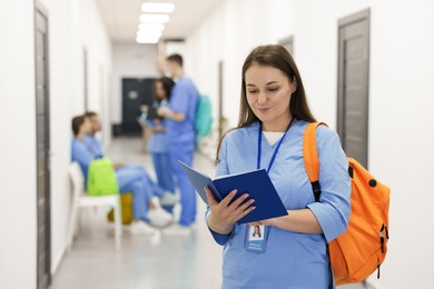 Photo of Medical student in uniform with backpack and notebook at university, selective focus