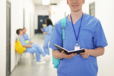 Photo of Medical student in uniform with backpack and notebook at university, selective focus