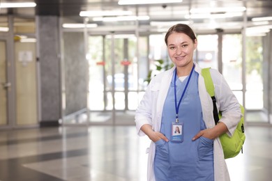 Photo of Medical student in uniform with backpack indoors, space for text