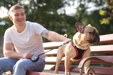 Photo of Happy man with his cute French bulldog on bench in park, selective focus