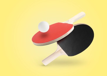 Image of Ping pong rackets and ball in air against yellow background